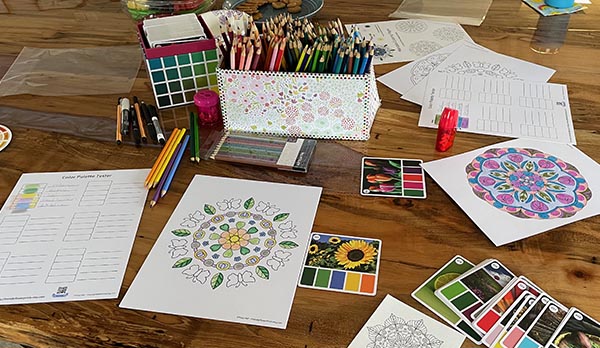 three coloring pages and a color palette tester with colored pencils and markers scattered around